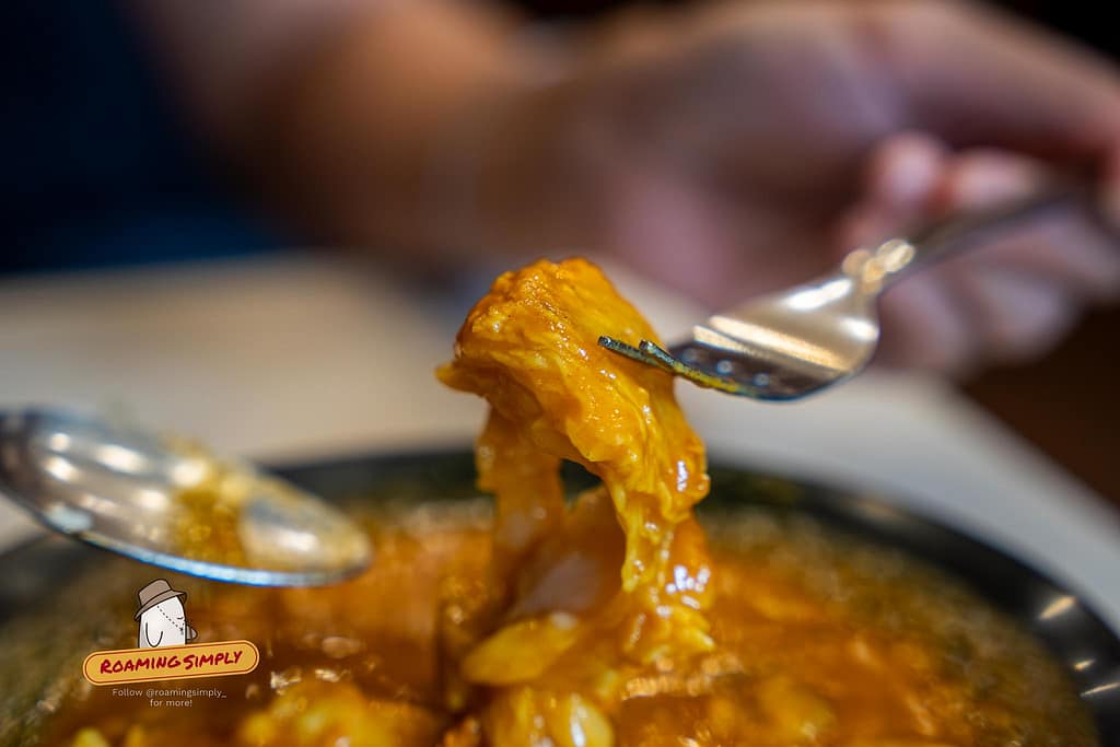 Close-up photograph of a fork lifting a hearty chunk of potato generously coated in thick, golden-orange dhal curry at Singapore Zam Zam, with the rest of the dish softly blurred in the background.