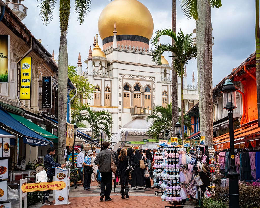 The golden dome of Sultan Mosque (Masjid Sultan) towering over the colorful shophouses and pedestrians on Bussorah Street in Kampong Glam, Singapore.