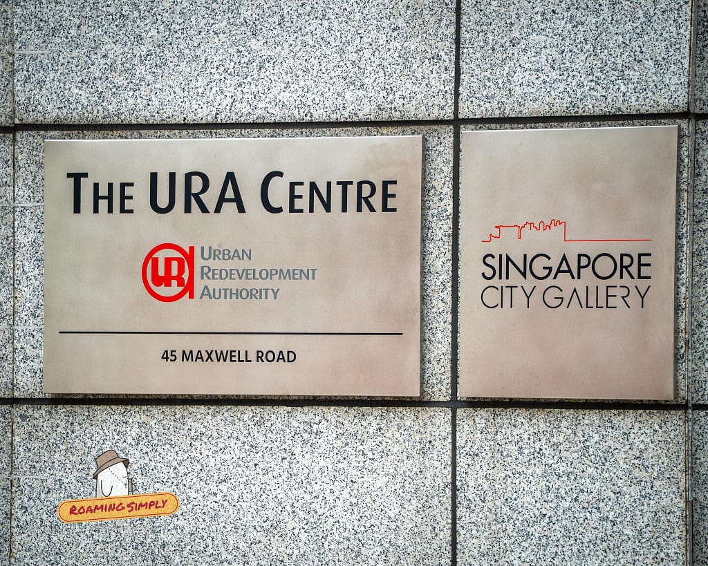 Close-up photograph of the metallic entrance signs for The URA Centre (Urban Redevelopment Authority) and the Singapore City Gallery mounted on a granite wall at 45 Maxwell Road.