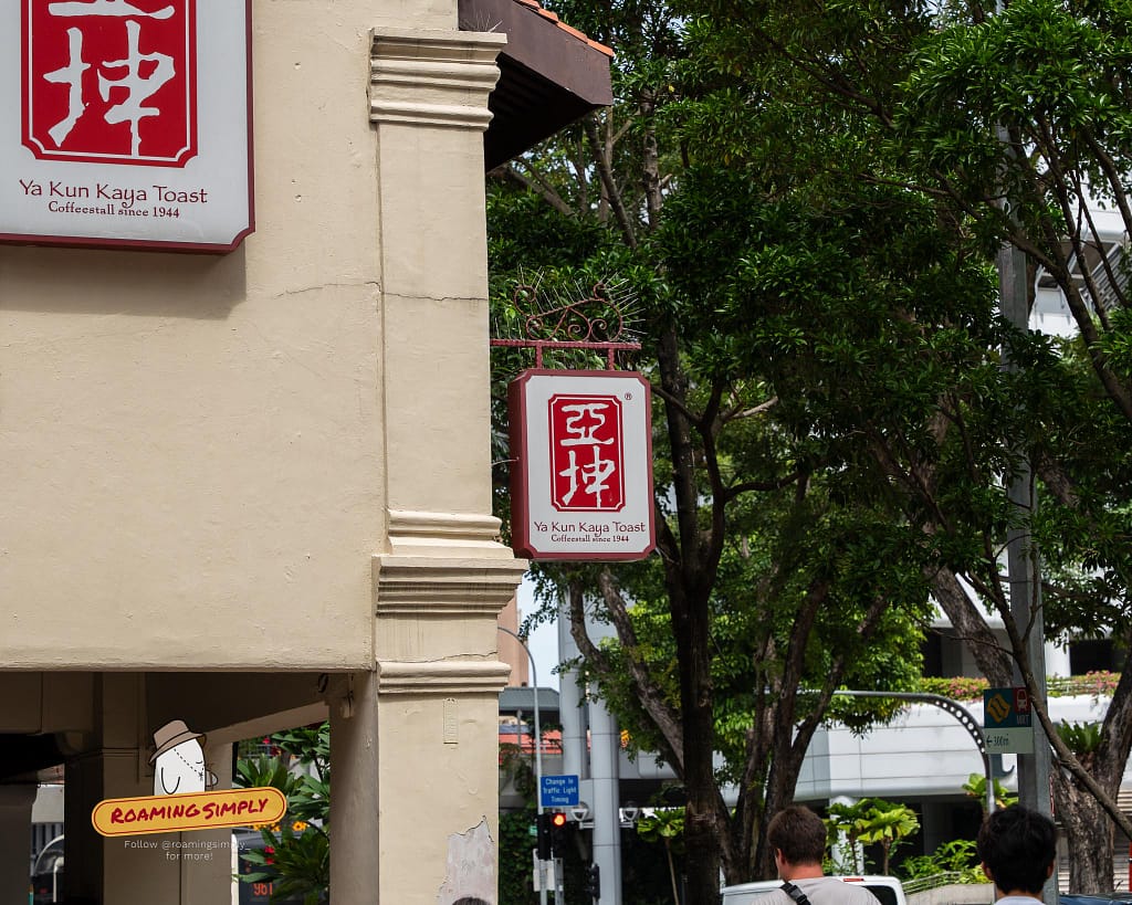 The iconic red and white Ya Kun Kaya Toast exterior sign hanging on a building pillar in Singapore.