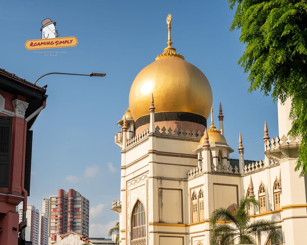 The prominent golden dome and striking white facade of the historic Sultan Mosque gleaming against a clear blue sky in Kampong Glam, Singapore.