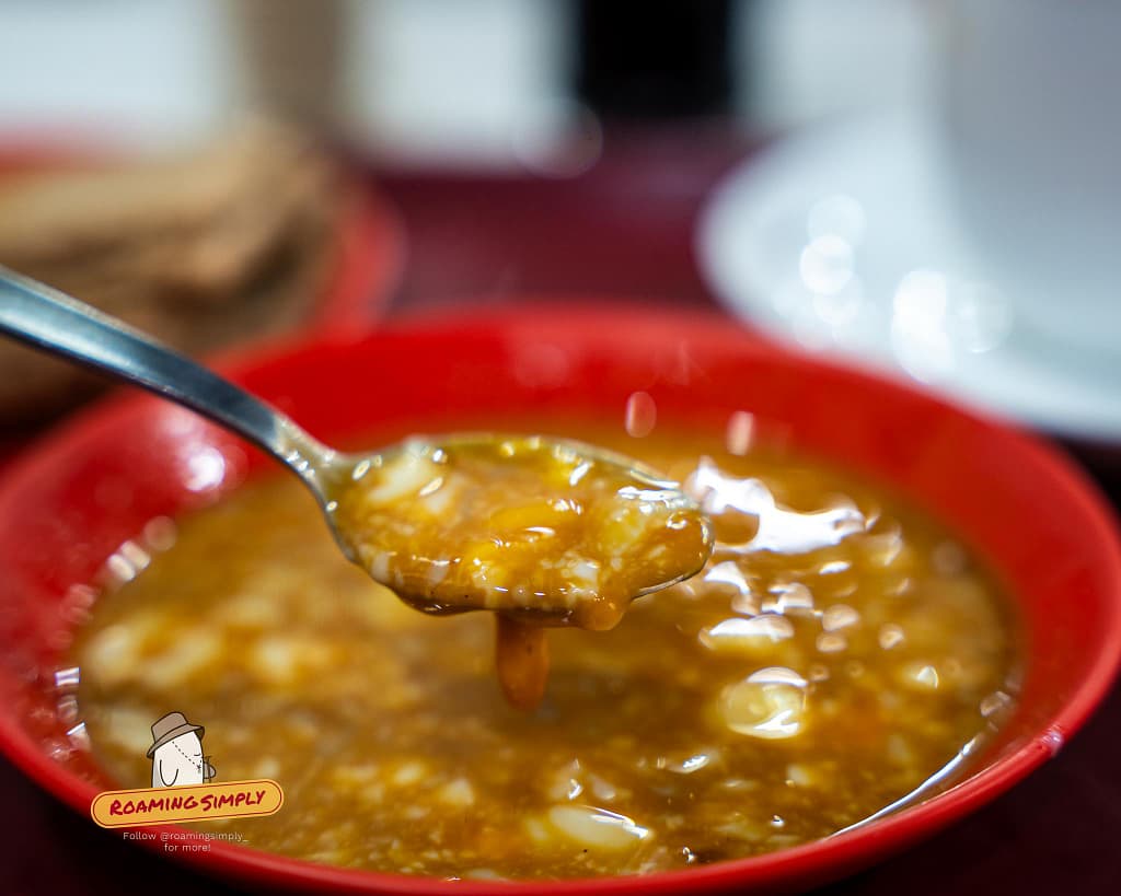 Close-up of mixed soft-boiled eggs with dark soy sauce and white pepper on a spoon at Ya Kun Kaya Toast in Singapore.