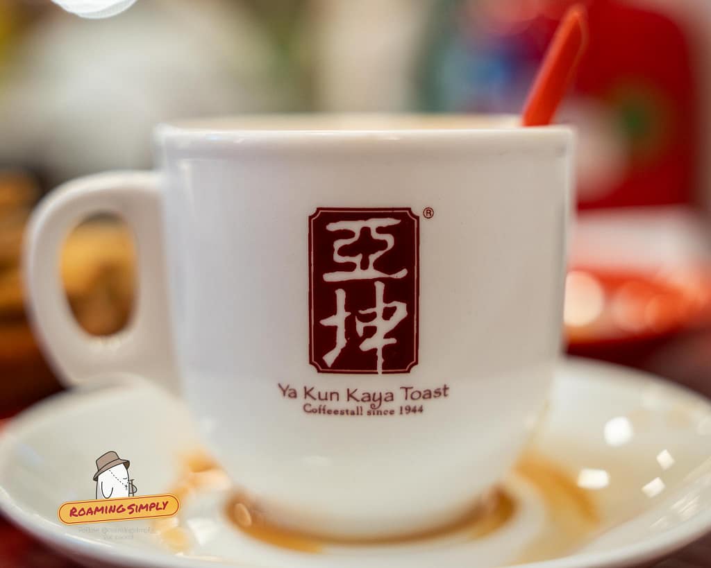 Close-up of a classic white Ya Kun Kaya Toast cup and saucer containing traditional hot Singaporean coffee or tea.