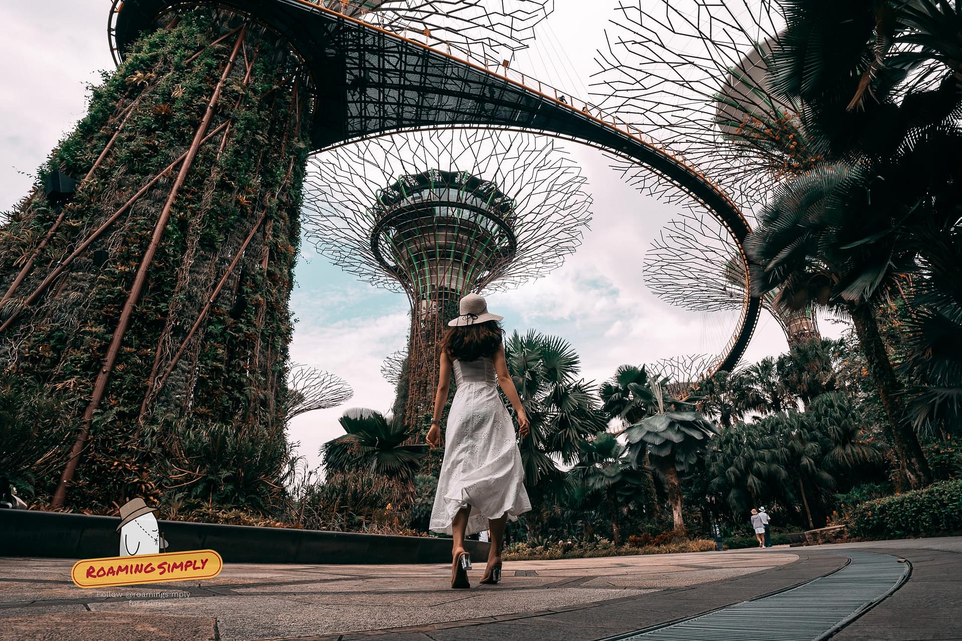 Low-angle view of a visitor walking beneath the massive vertical gardens of the Supertree Grove and the OCBC Skyway at Gardens by the Bay in Singapore.
