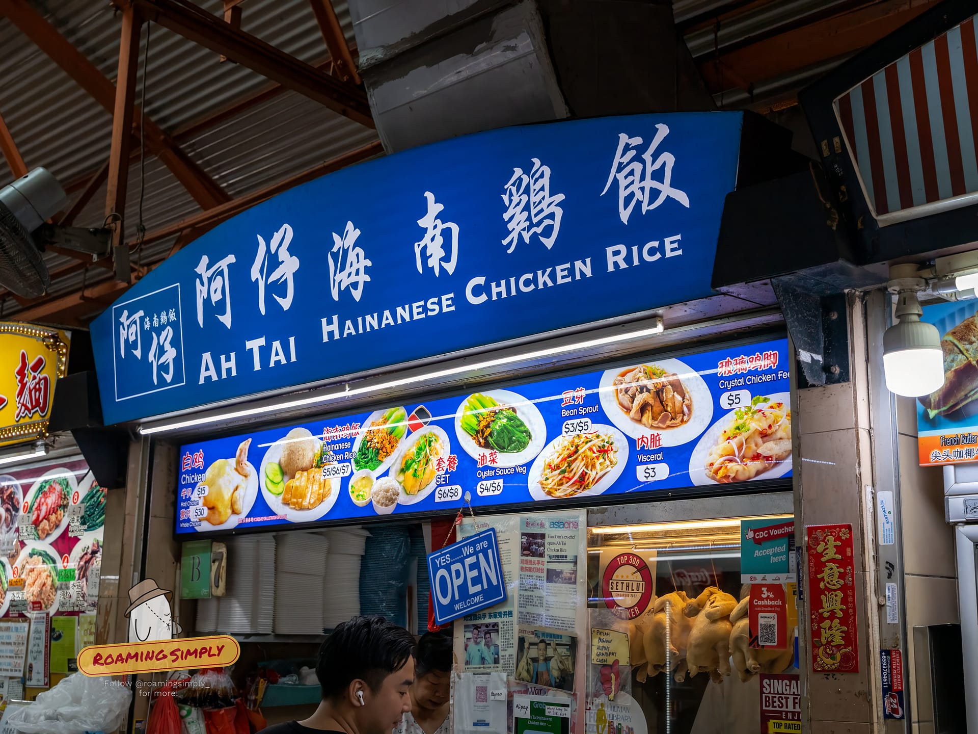 Blue signboard of Ah Tai Hainanese Chicken Rice at Maxwell Food Centre, displaying menu photos, prices, and Chinese characters above the stall window.