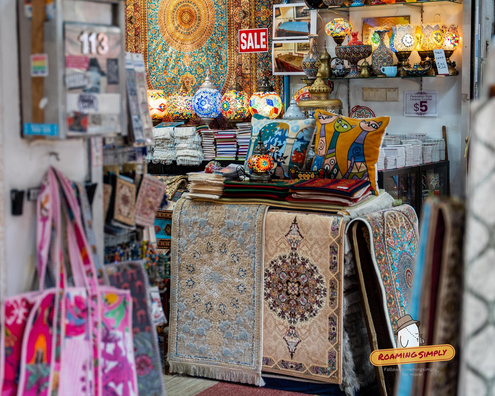 A colorful shop display in Kampong Glam, Singapore, featuring lit Turkish mosaic lamps, intricate rugs, and various souvenirs.