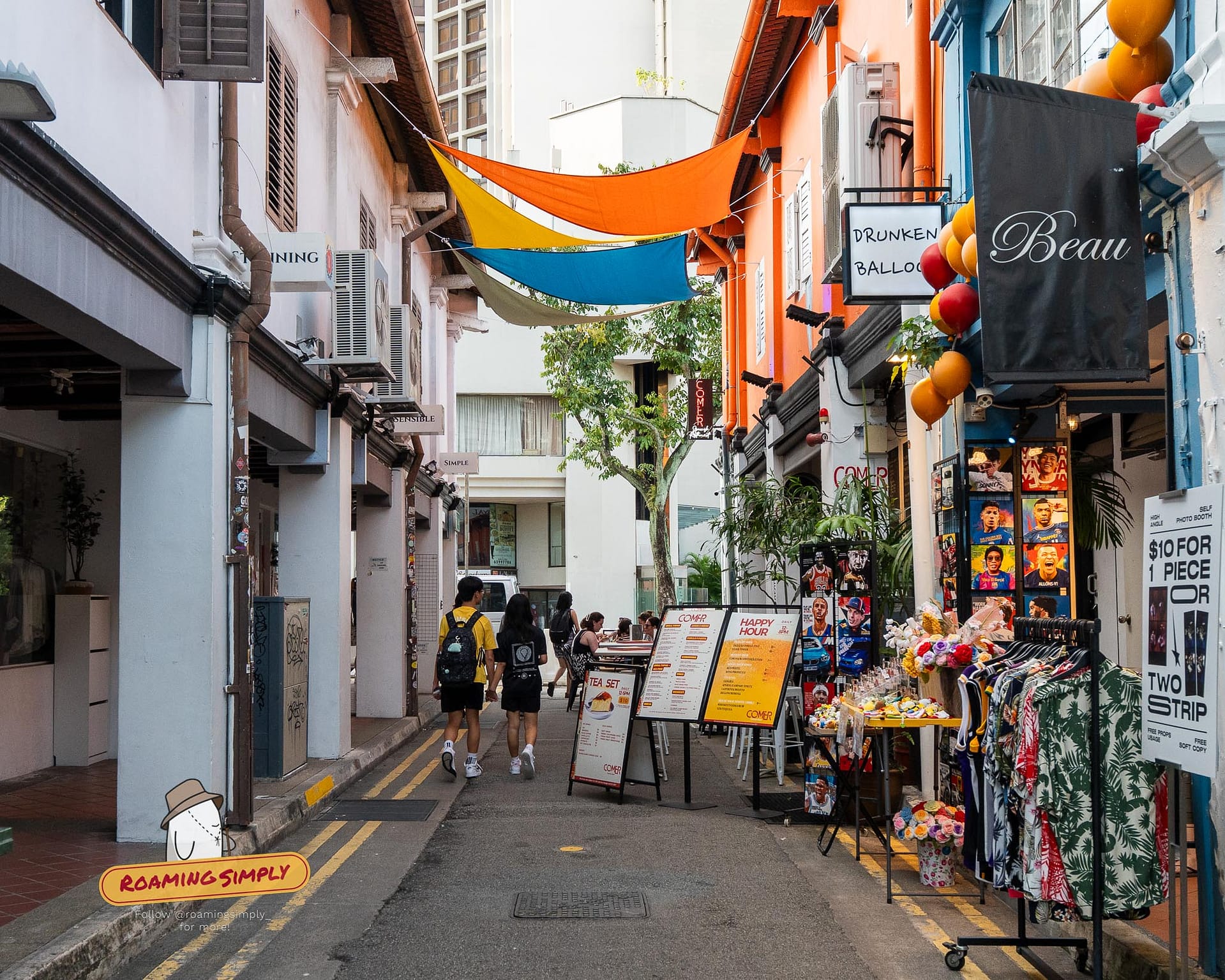 People walking down the vibrant, narrow street of Haji Lane in Singapore, lined with colorful boutiques and cafes under overhead sun shades.