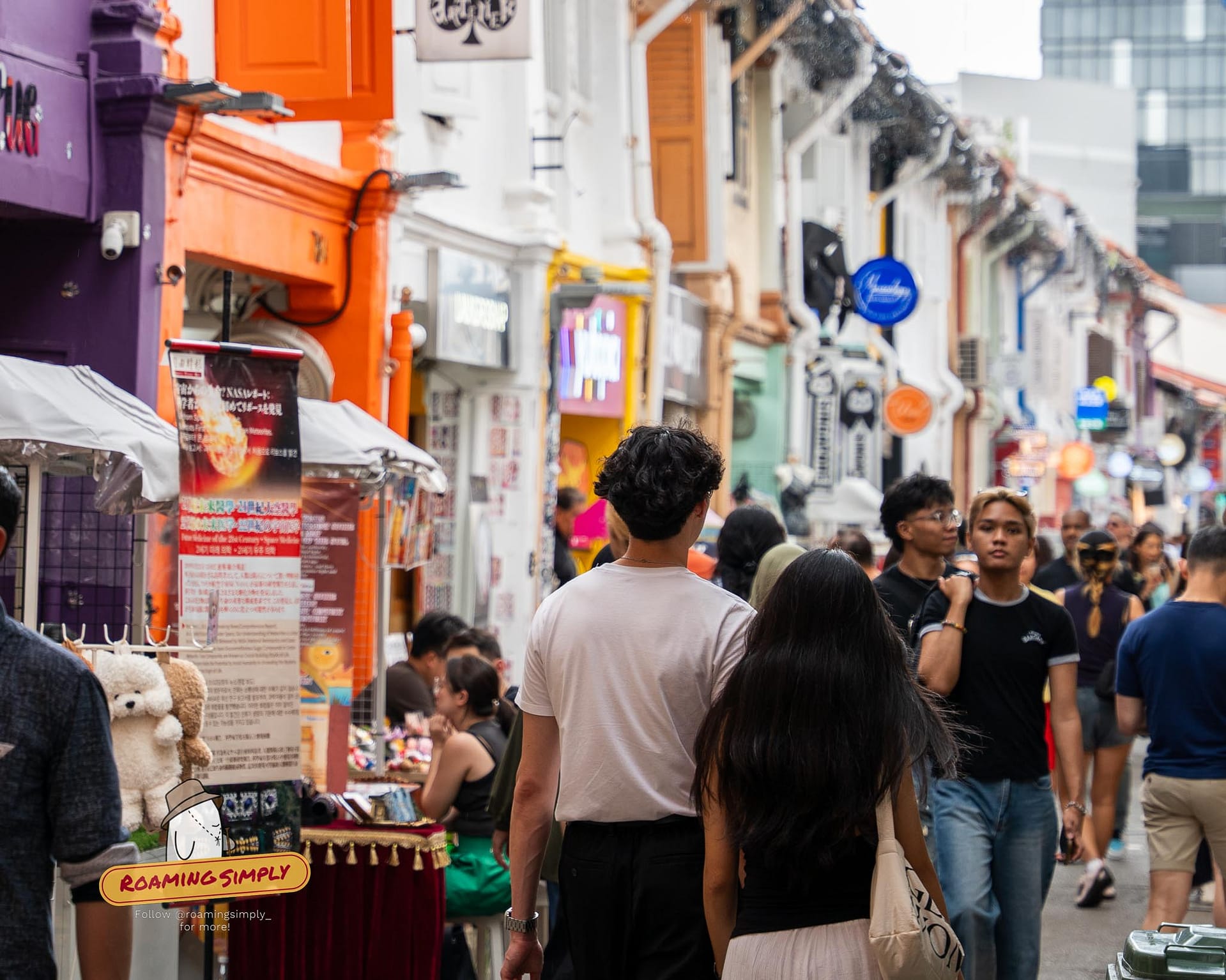 Crowds of people walking past colorful indie boutiques and street stalls on the narrow alleyway of Haji Lane in Singapore.